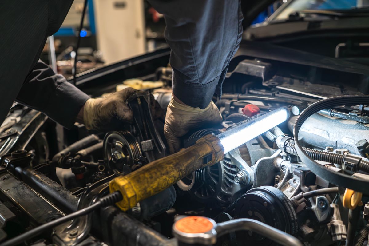 Technician using a work light to trace a problem in an engine bay